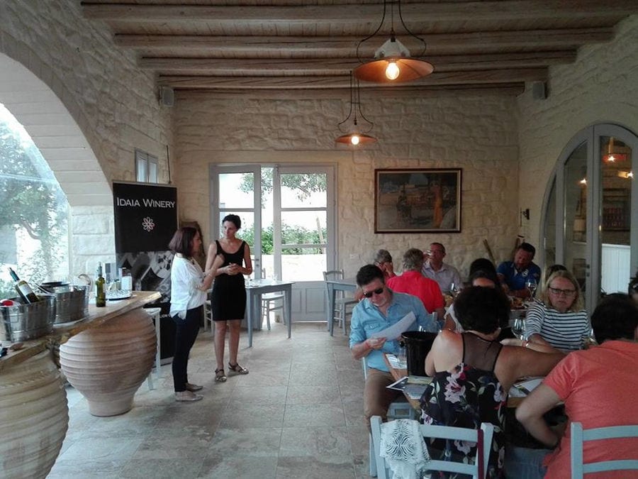 guide discussing with one woman and tourists sitting on the tables and enjoy a wine tasting at Idaia Winery